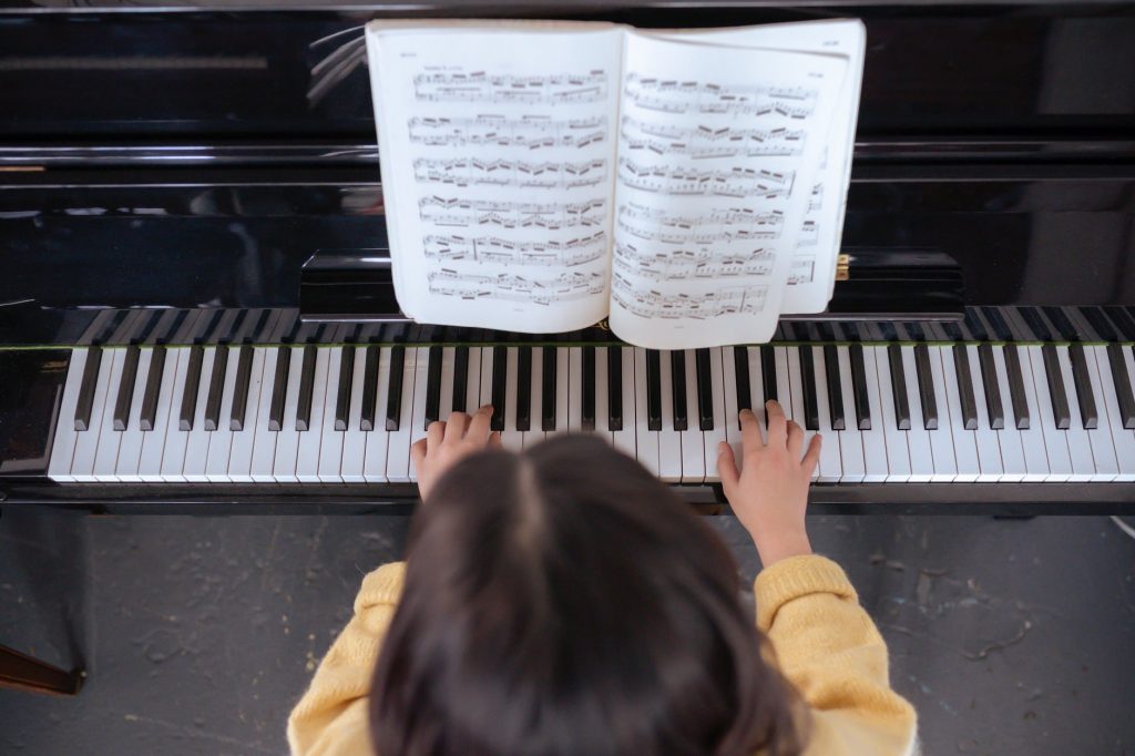 faceless lady practicing on piano near music book in room