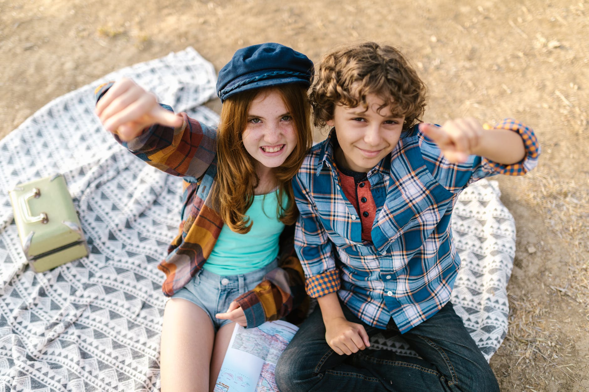 overhead shot of two teens sitting on picnic blanket while looking at camera