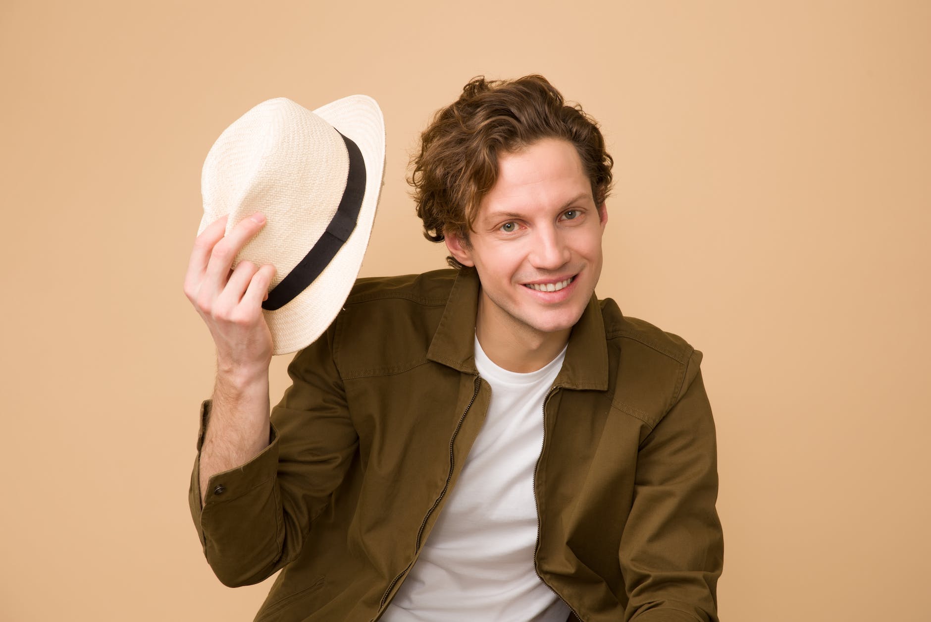 man wearing brown dress shirt holding white fedora hat